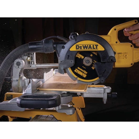 DEWALT circular saw cutting wood on a miter saw table with dust extraction attachment in action.