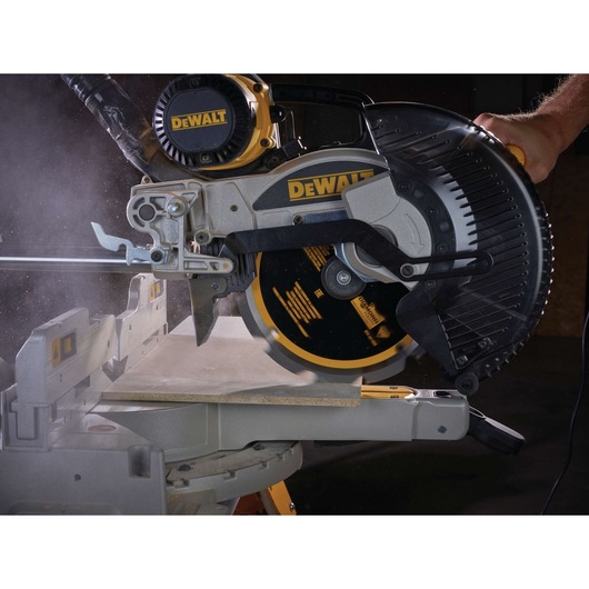 A DEWALT branded power saw in action cutting a piece of material, with visible dust and debris being generated. The saw is