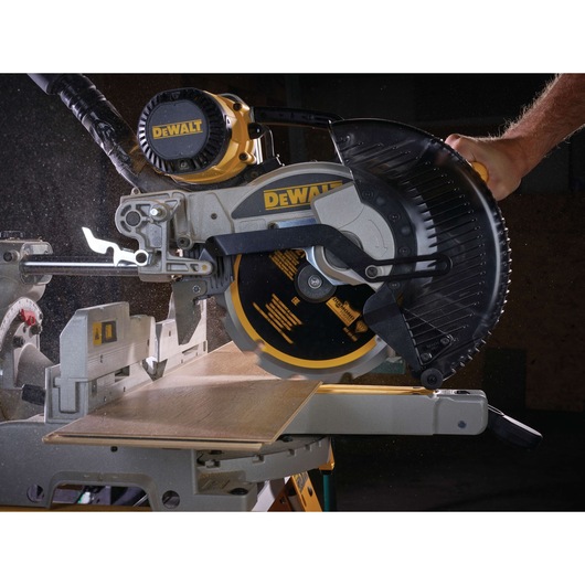 A DEWALT miter saw in use, cutting a piece of wood with visible sawdust, demonstrating the saw's precision and power.