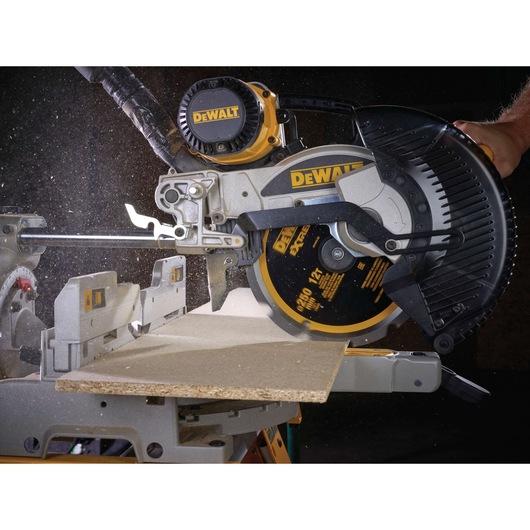 A close-up view of a DEWALT miter saw cutting through a piece of wood, with sawdust flying during operation.