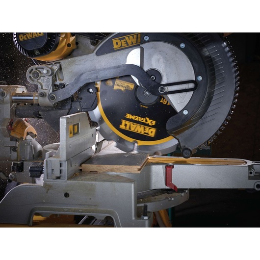 Close-up of a DEWALT DT1475 saw blade installed in a miter saw cutting through a piece of wood. The saw is in action, with