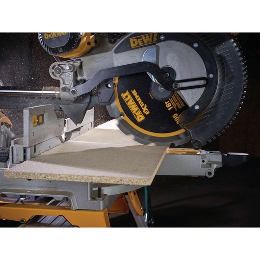 A close-up of a DEWALT mitre saw cutting a piece of wood, with sawdust flying as the blade rotates.