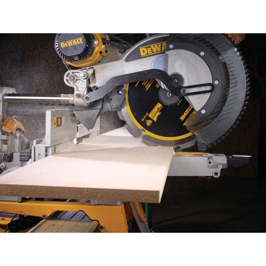 A DEWALT miter saw cutting a piece of wood, with sawdust visibly flying during operation.
