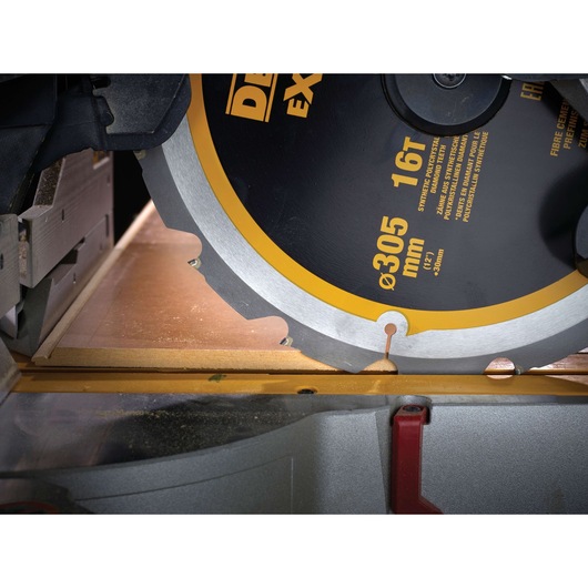 Close-up of a DEWALT 305mm circular saw blade cutting a wooden board, showing detailed teeth and branding.