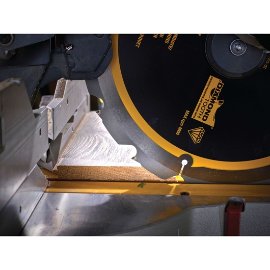 Close-up of a DEWALT circular saw blade cutting a wooden board on a mitre saw.