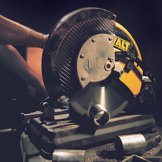 A DEWALT branded metal cutting saw in use, cutting through a metal pipe. There is a person's arm operating the saw, and