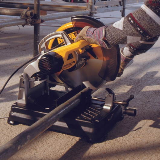 A DEWALT DT1927 power saw being used to cut a metal pipe on a construction site. The saw is mounted on a sturdy base and is
