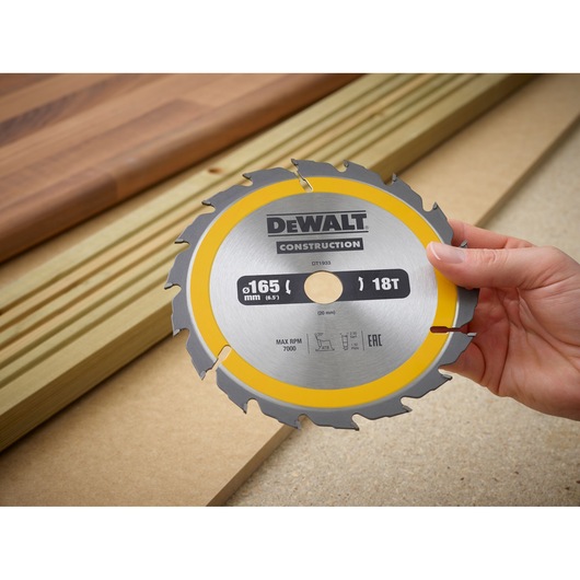 Hand holding a DEWALT DT1933 circular saw blade with 165mm diameter on a wooden surface.