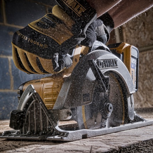 A close-up of a DEWALT cordless circular saw in use, cutting through a wooden plank. The person operating the saw is wearing