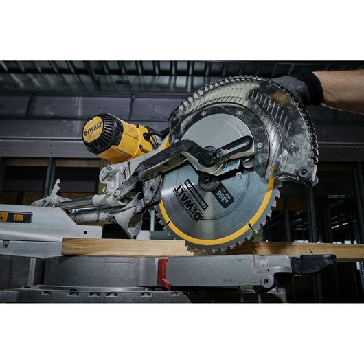 A close-up of a DEWALT circular saw cutting a piece of wood in a workshop setting. The saw blade and motor are prominently