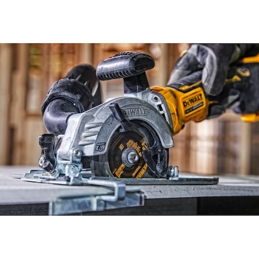 A DEWALT circular saw is being used to cut a sheet of material. The saw is held by a gloved hand, and the DEWALT logo is