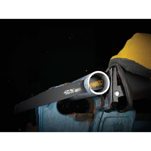 DEWALT saw blade cutting through a metal pipe, held by a gloved hand against a dark background.