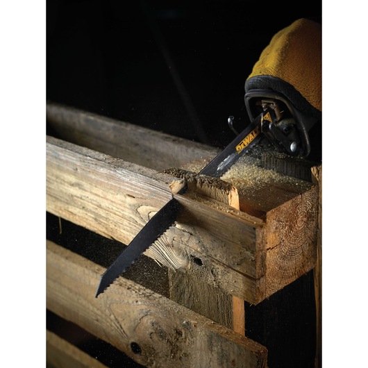 A DEWALT reciprocating saw blade cutting through a wooden pallet, with sawdust flying as the blade moves.