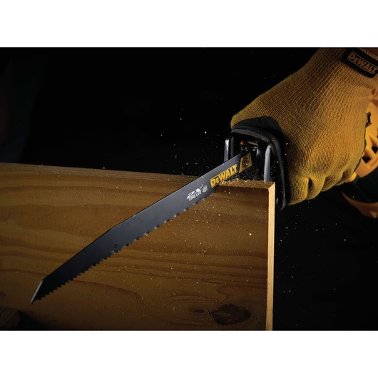 Gloved hand uses a DEWALT saw blade to cut through a wooden plank, with sawdust visible.
