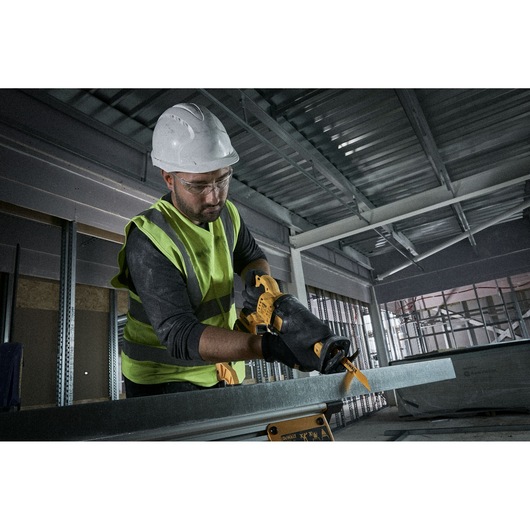 A person wearing a safety helmet, high-visibility vest, and gloves is using a DEWALT reciprocating saw with a yellow blade