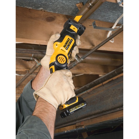 A person wearing work gloves holds a DEWALT cordless reciprocating saw and cuts a metal pipe in a construction or repair