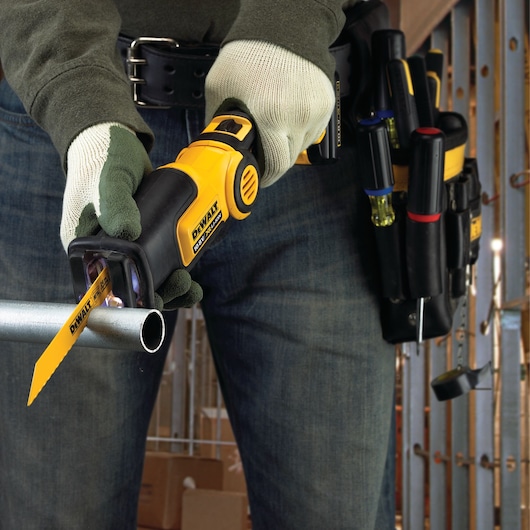A person wearing gloves is using a DEWALT reciprocating saw with a yellow DT2354 blade to cut through a metal pipe. The