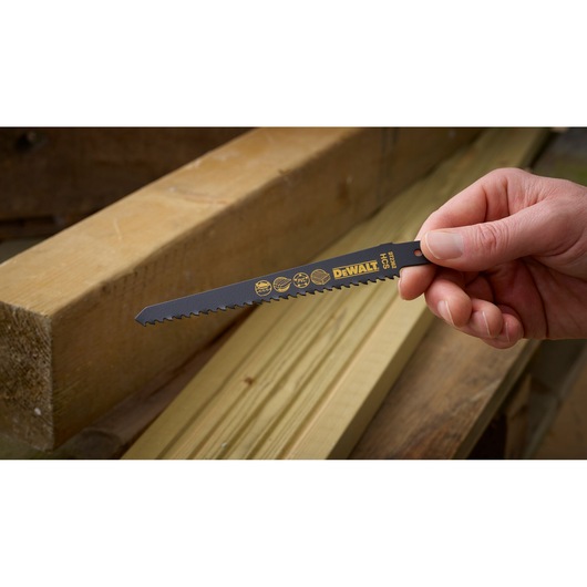 Hand holding a DEWALT DT2362 saw blade, shown next to wooden planks in a workshop setting.