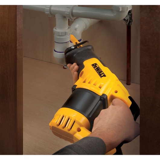 Hands using a DEWALT reciprocating saw to cut plastic pipes under a sink.