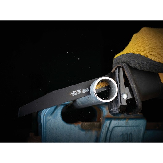 Close-up of a DEWALT reciprocating saw cutting through a metal pipe, with a gloved hand holding the tool and metal shavings