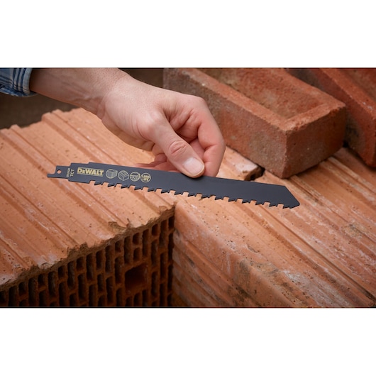 Hand holding DEWALT DT2420 saw blade, shown next to several red bricks arranged for demonstration.