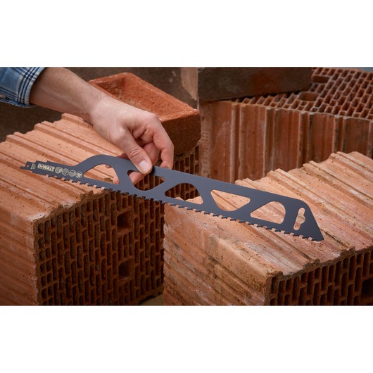 A hand holding a DEWALT saw blade, designed for cutting bricks, with several red bricks stacked in the background.
