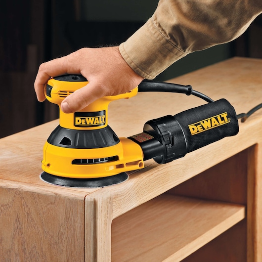 A person using a DEWALT electric sander to smooth the surface of a wooden piece of furniture.