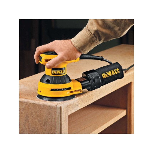 DEWALT sander being used to smooth wood furniture with a hand holding the tool.