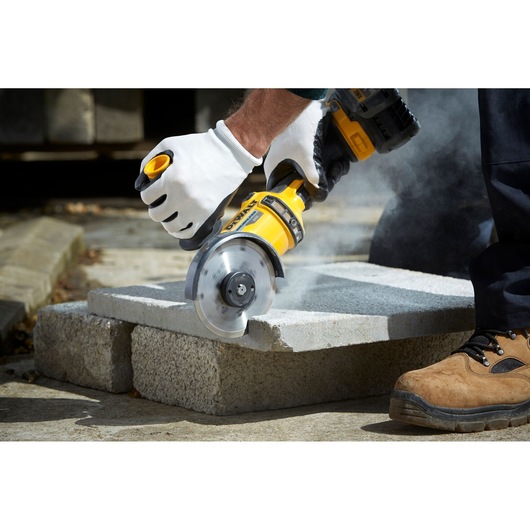 Person uses DEWALT angle grinder to cut a concrete slab, wearing gloves and safety footwear.