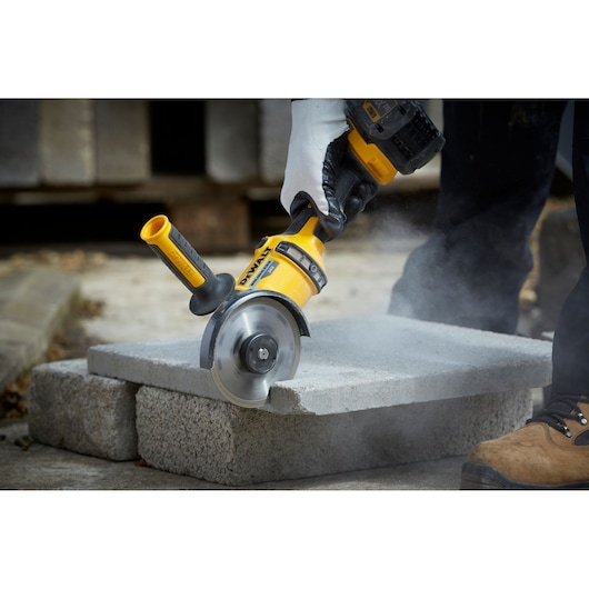 A close-up of a DEWALT angle grinder being used to cut concrete blocks. The tool is held by a person wearing gloves, and
