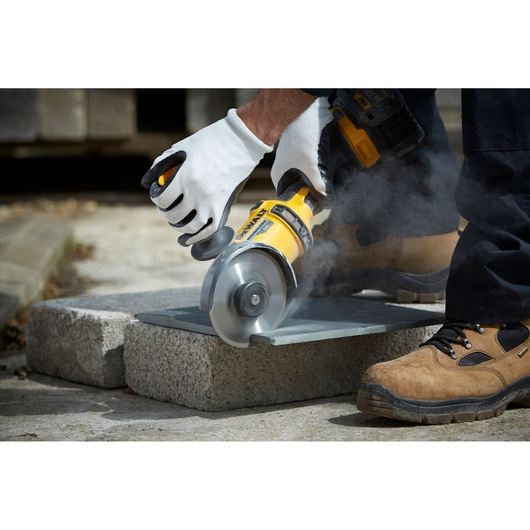 A close-up of a person using a DEWALT power tool with a circular blade to cut a stone slab outdoors. The person is wearing
