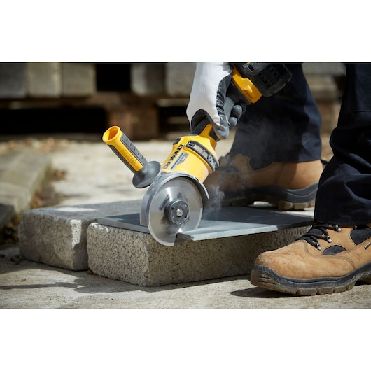 DEWALT angle grinder cutting a tile outdoors, operated by a person in safety gloves and boots.