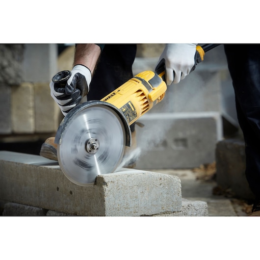 A person wearing gloves uses a yellow DEWALT power tool with a circular blade to cut a concrete block outdoors.