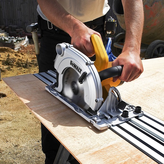 A DEWALT circular saw is being used to cut a wooden board along a metal guide rail outdoors.