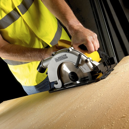 Person using a DEWALT circular saw to cut wood, wearing a yellow safety vest.