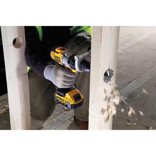 Person using DEWALT drill to make a large hole in a wooden beam, wood chips flying out.