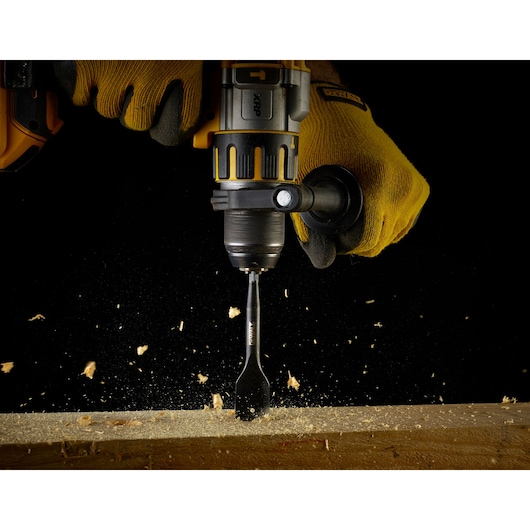 DEWALT drill with DT4768 spade bit drilling into wood, worn by gloved hands with wood shavings flying.