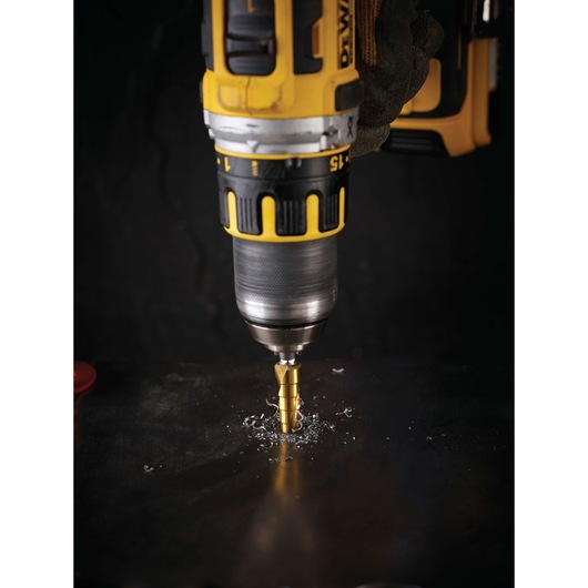 A close-up of a DEWALT drill being used with a step drill bit to create a hole in a metal surface. Metal shavings are