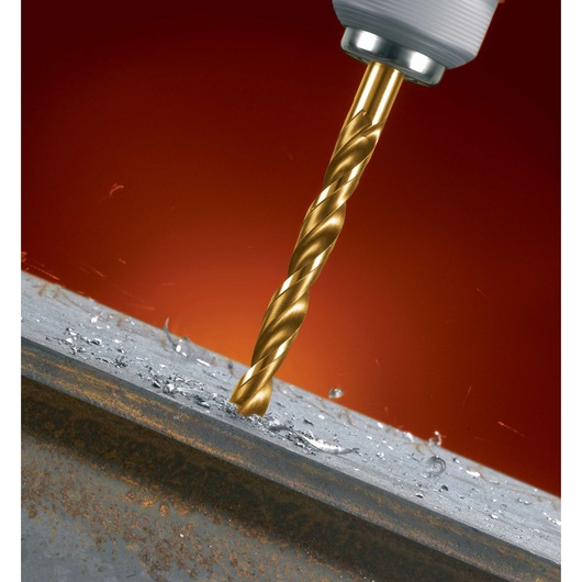 A close-up of a golden twist drill bit drilling into a metal surface, with metal shavings scattered around the hole.