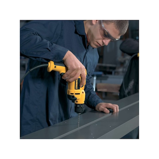A person using a yellow DEWALT electric drill to make holes in a metal surface in an industrial or workshop setting.