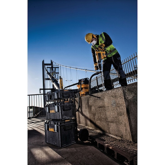 A worker wearing a yellow hard hat, safety vest, and face mask is using a yellow DEWALT power tool on a construction site