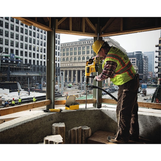 A construction worker using a yellow DEWALT power tool to drill into a concrete surface at a building site in an urban area