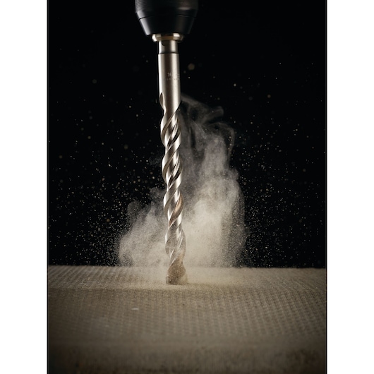 Close-up of a drill bit attached to a power drill, as it drills into a concrete or stone surface, creating a cloud of dust.