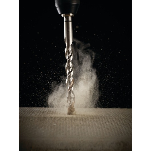 A close-up image of a DEWALT drill bit attached to a drill, actively drilling into a surface with dust particles rising up.