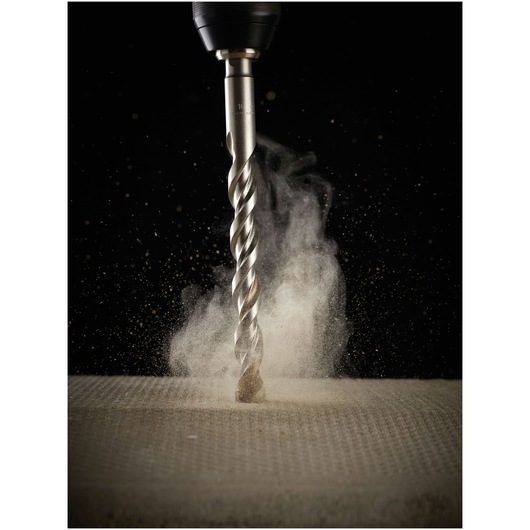 A close-up view of a DEWALT drill bit creating dust as it drills into a textured concrete surface.