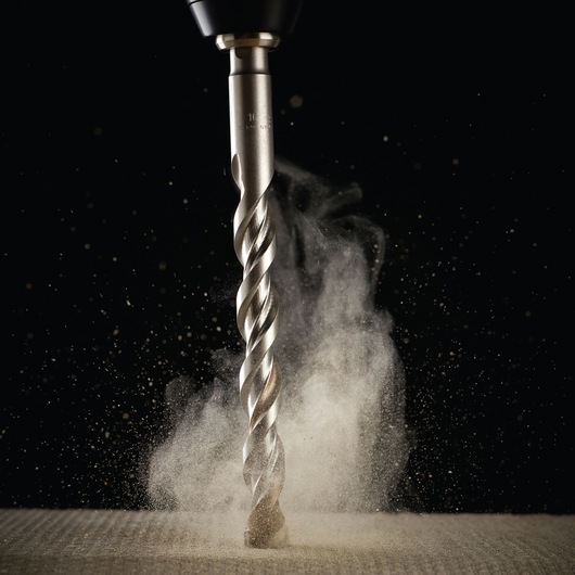Close-up of a metal drill bit in action, creating dust as it drills into a surface against a dark background.