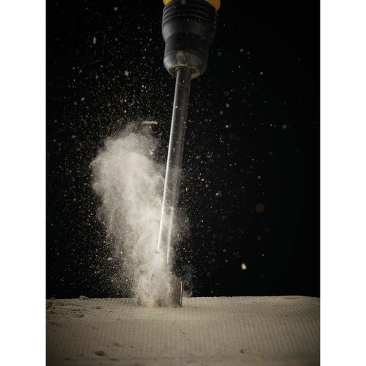 A DEWALT chisel tool striking a concrete surface, causing dust and debris to scatter, shown against a black background.