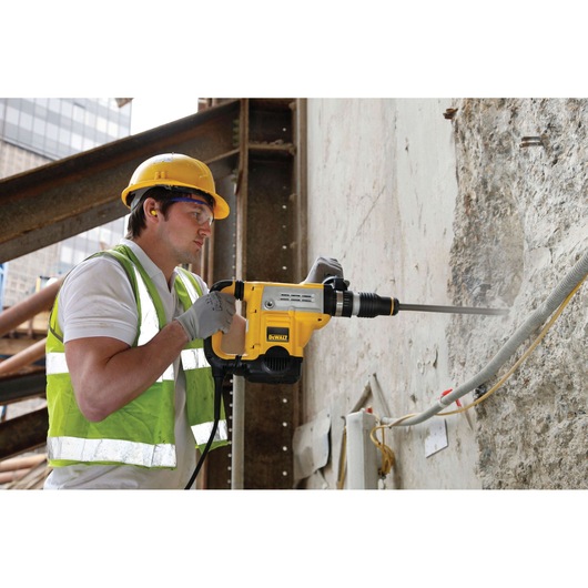 A construction worker wearing a yellow hard hat and reflective vest uses a DEWALT DT6825 power tool to drill into a concrete