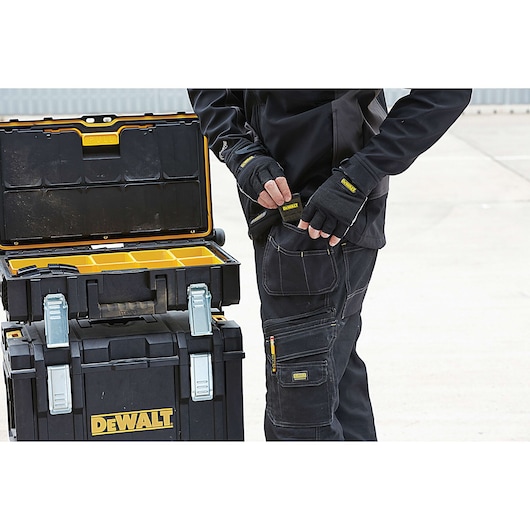 Person with DEWALT gloves standing beside open DEWALT tool storage boxes on a concrete surface.