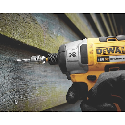 A close-up image of a DEWALT cordless 18V XR brushless impact driver being used to drive a screw into a wooden surface. A